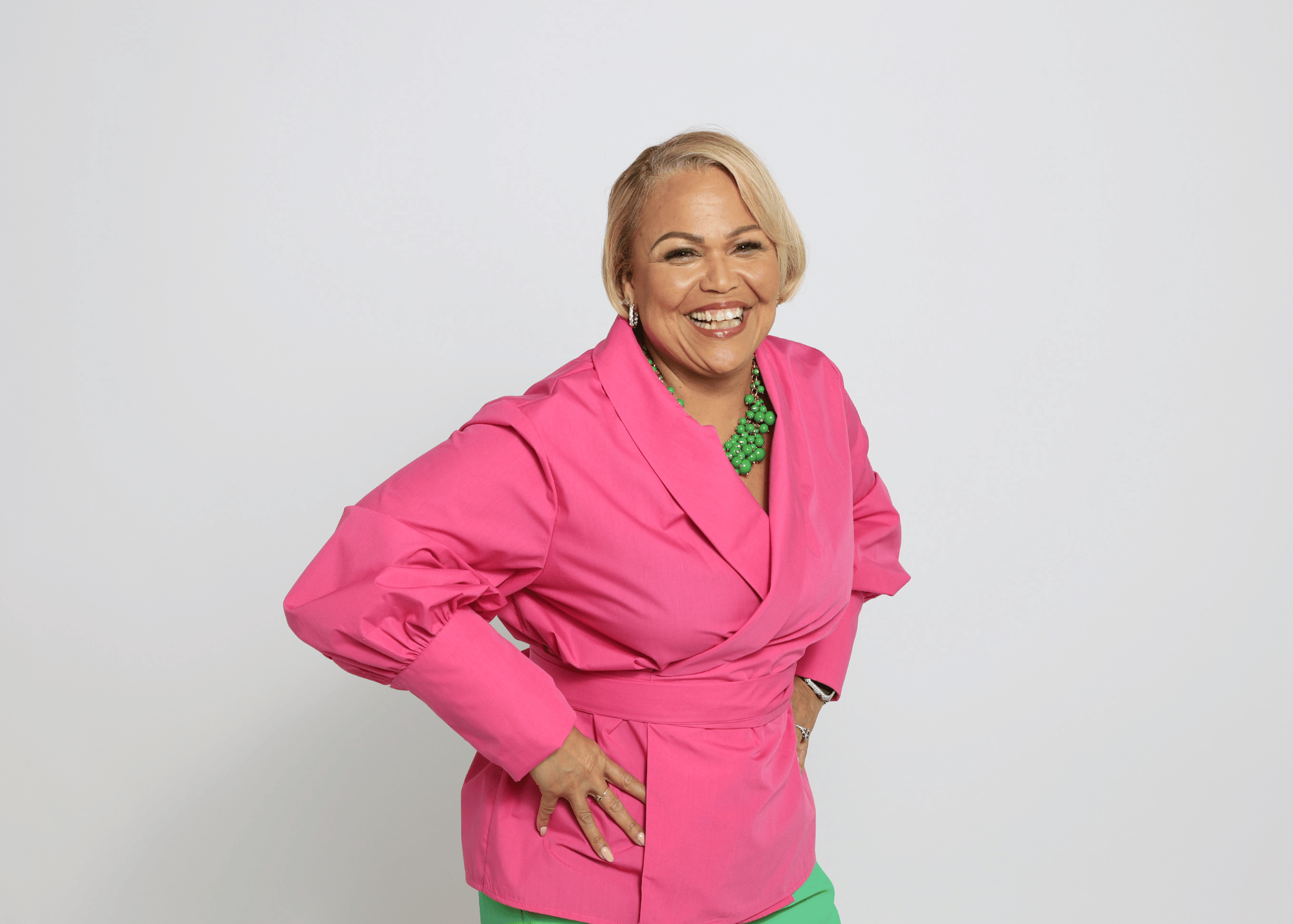 Dr. Vicki Wright Hamilton, a strategic business and leadership coach, smiling confidently in a vibrant pink blazer and green accessories.