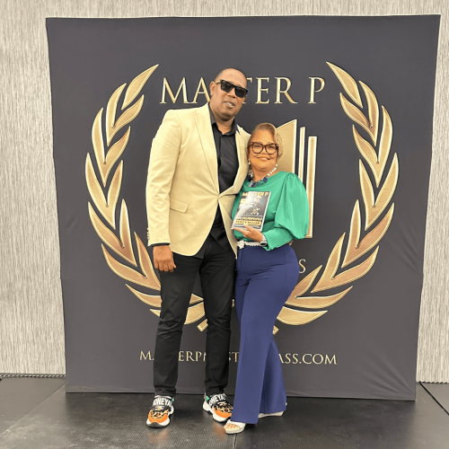 Dr. Vicki Wright Hamilton stands on stage with Percy "Master P" Miller, both holding a copy of "Mastering Wealth: Volume 2 Purpose," during a promotional event.